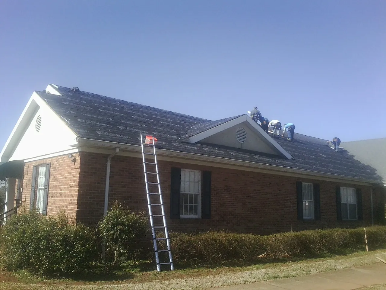 Crew tearing shingles off a brick ranch roof with a ladder set — Emergency Roof Repair work by our crew in Harrington Park