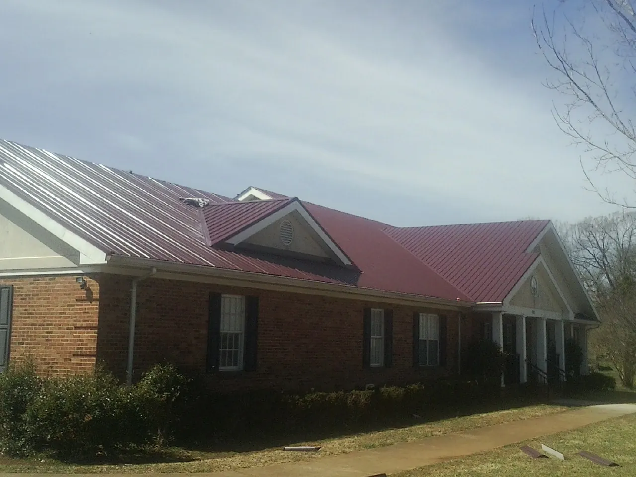 Red metal roof with gabled entries on a long brick building, from a Hail Damage Roof Repair job in Harrington Park