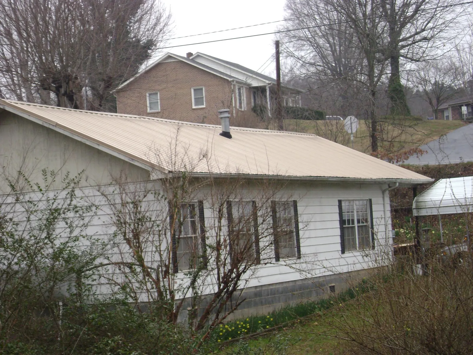 Tan metal roof on a white sided house set into a hillside — Commercial Roofing by Roofing Brothers in Harrington Park